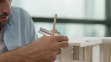 Akıllı inşaat mühendisinin el ölçümü ev modeli inşaatı. Gündelik kıyafetlerle profesyonel mimar bina inşaatı planlarken ev modeline bakıyor. Eline odaklan. İzleme