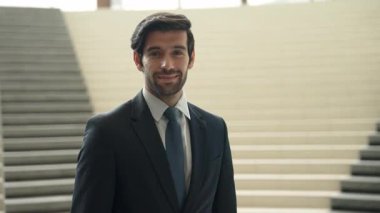Akıllı iş adamı merdivenlerde kameraya bakıyor. İş elbisesi giyerken kameraya gülümseyen başarılı adamın yakın çekimi. Yönetici, kameraya bak. Hareket eden kamera. Sevinçli..