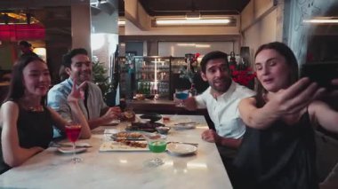 Sefie 'yi akıllı telefondan alan bir kadın, arkadaşlarıyla birlikte özel kokteyl içecekleriyle poz veriyor. Etrafı ızgara ve kızarmış et menüsüyle çevrili. Restoranda özel bir şef masası menüsü bulunuyor. Vinosity.