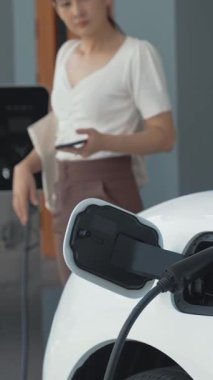 Evinde şarj edilen elektrikli bir araçla işten yeni dönen modern bir kadının ilerici yaşam tarzı. Elektrikli araç, sürdürülebilir temiz enerjiyle çalışıyor..