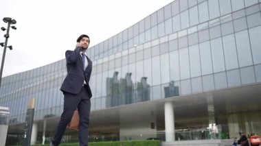 Akıllı iş adamı binada yürürken telefonla konuşuyor. İş planı, pazarlama stratejisi ya da çalışma hakkında konuşmak için akıllı telefonla konuşurken sokakta yürüyen mutlu bir yönetici. Sevinçli..