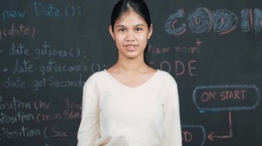 Genç öğrenci başarılı planını kutlarken kolunu kaldırdı. Mühendislik koduyla karatahtaya bakarken kameraya bakan mutlu genç, STEM sınıfında yazılı. Öğretim