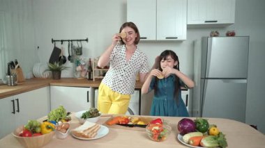 Zeki beyaz anne ve Asyalı kız birlikte yemek pişiriyor ve sebze doğruyor ya da akşam yemeği için salata hazırlıyor. Mutlu anne ve kız taze yemekle sağlıklı yemek yapıyorlar. Sağlıklı gıda konsepti. Pedagoji.