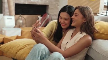 Lezbiyen aşığın elinde telefonla oturma odasındaki kanepede yatarken fotoğraf çekiyor. Çekici kız arkadaş ya da oda arkadaşı birlikte zaman geçirip modern odada selfie çekiyorlar. İlişki. Myrmidon.