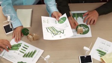 Eko evi projesini yel değirmeni tasarım modeli ve karbon ayak izini azaltmak için yeşil enerji kullanım grafiği ile toplantı masasında tartışan harika bir iş ekibi. Dünyayı kurtarın. Eline odaklan. Tanımlama.