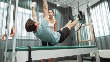 Eğitmen rehberliğinde Pilates Cadillac 'ta ters bacak yükseltme pratiği yapan sağlıklı bir müşteri. Çekirdek dayanıklılığını ve üst vücut dengesini arttırmak için Cadillac 'ı geren adam. Alışkanlık.