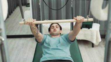 Adam spor salonundaki kol ve vücut kaslarını güçlendirmek için pilates trapez çubuğunda çekirdek egzersizi yapıyor. Göğüs ve omuz güçlendirmek için Cadillac 'a göğüs presi yapan antrenör. Alışkanlık.