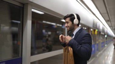 Tren platformda hareket ederken akıllı proje yöneticisi kulaklıktan müzik dinliyor. Kafkasyalı iş adamı kulaklık kullanıyor. Platformda beklerken rahat müzik dinliyor. Çalışma rutini. Sevinçli..