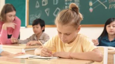 Sınıfta mutlu bir çok kültürlü öğrenci ilkokulda sınıfta sınav yaparken ya da not yazarken beyaz çocuk kameraya gülümsüyor. Eğitim konsepti. Pedagoji.