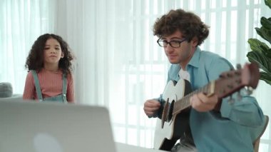 Çekici beyaz bir baba gitar çalarken tatlı bir kız müzik eşliğinde dans ediyor. Mutlu baba ve Amerikalı kız birlikte vakit geçirirken akıllı çocuk müzik yapıyor. Aile eğlence konsepti. Pedagoji.