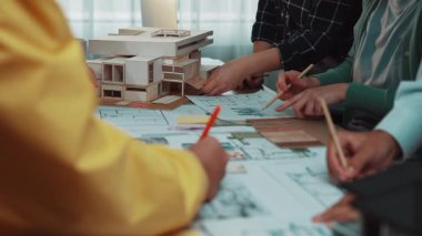 Canlı bir işbirlikçi tasarım oturumunda mimarlar ve müşteriler aktif olarak bina planları ve modellerini tartışıyor. Sahne, profesyonel bir çalışma alanında takım çalışmasının ve yaratıcılığın altını çiziyor. SACTR