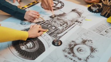 Çalışma alanındaki mekanik motor modeli bir çizimle uğraşan elleri resmeden ortak bir sahne. Araçlar ve dişliler, yaratıcılığı ve takım çalışmasını gösteren detaylı tasarımı çevrelemektedir. SACTR