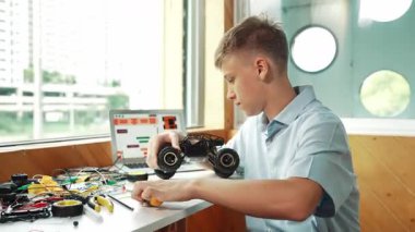 Elektronik teçhizat kullanırken robot modelini tamir eden mutlu bir genç etrafta kablo ve dizüstü bilgisayarla araba tekerleğini çıkartıyor. Akıllı çocuk ders çalışıyor ya da sınıfta robot araba yapımını öğreniyor. Öğretim