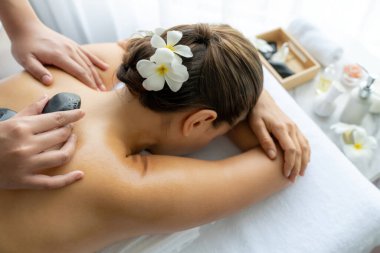 Lüks tatil köyündeki kaplıcalarda sıcak taş masajı. Gün ışığı sükunet ortamında, mutlu kadın müşteri bazalt taş masajından zevk alıyor. Rahatlatıcı bir sıcaklıkla vücudun üzerinde süzülüyor. Sessiz.