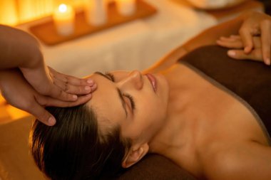 Beyaz kadın stres önleyici kafa masajı yapmaktan ve lüks otel veya otelde sıcak mum ışığında yüz güzelliği eğlencesi yapmaktan zevk alıyor. Sessiz.