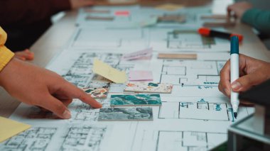 Ekip planlama oturumunda el ele tutuşup çizimler ve görsel yardımlarla mimari bir düzene işaret ediliyor. Katılımcılar proje fikirleri üzerinde aktif olarak işbirliği yapıyorlar. SACTR