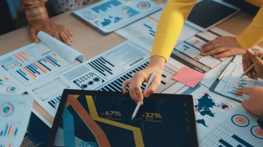 Çeşitli bir işletme ekibi, bir ofiste yapılan stratejik planlama toplantısında içgörü için tablet kullanırken, finansal analizler, tablolar ve verileri gözden geçirme konusunda işbirliği yapmaktadır. SACTR