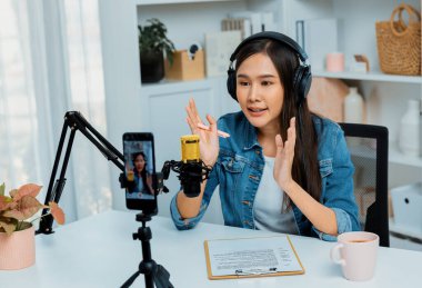 Asyalı sunucu canlı yayında canlı yayında canlı yayında sosyal medyada kulaklık takarak konuşuyor. Dinleyicileri modern stüdyoda koçluk yaparak selamlıyor. Taktik.