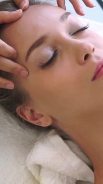 Lüks bir spa merkezinde masaj terapisti tarafından yüz masajı ve spa tedavisi için kaplıcaya uzanmış rahat bir kadın. Sağlık, stres atma ve gençleştirme kavramı.