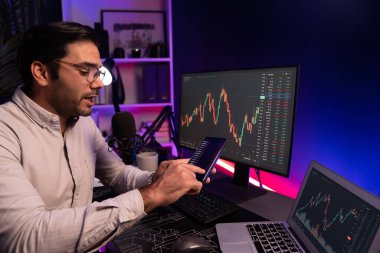 Akıllı tüccar akıllı iş adamı akıllı telefonu kullanarak modern evde kâr amaçlı finans teknolojisi ile neon ışık ofisindeki bilgisayarda dinamik borsa yatırımlarını araştırır ve analiz eder. Tahmin et..