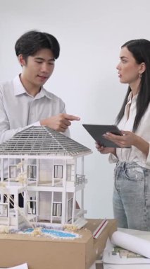 Güzel, genç, Kafkas proje yöneticisi Asyalı mühendis, mühendis ev modelini planlı, mimari ekipmanlarla toplantı masasında ölçerken tablet kullanarak kısaca Asyalı mühendis. Tertemiz.