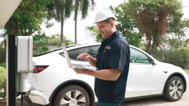 Evde EV şarj istasyonu kurulumu üzerinde çalışan nitelikli teknisyen, EV için dizüstü bilgisayarla şarj sisteminde sorun çıkarma ve yapılandırma ayarları yapıyor. Titiz