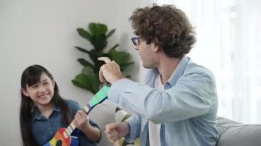 Beyaz bir baba akustik müzik dinlerken tatlı bir kız gitar çalıyor. Sevgili baba ukulele kullanırken şarkı söyleyerek dans ediyor. Yetenekli öğrenci de müzik öğreniyor. Yaratıcı aktivite konsepti. Pedagoji.