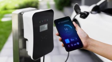 Akıllı telefon ekranı akıllı EV mobil uygulama üzerinde pil durumu EV araba garajdaki ev şarj istasyonu ile elektrik şarj ederken. Geleceğin yenilikçi EV arabası ve enerji sürdürülebilirliği. İnceleyin