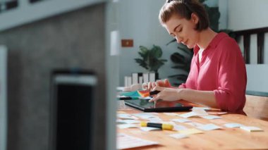 Tablet ekran logosu tasarımı ile toplantı masasında otururken renkli yapışkan notlar üzerine tasarımcı yazma fikrinin üst görünümü. Tasarım yapan ve karar veren profesyonel bir iş kadını. Sempozyum.