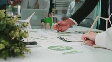 İş adamları çizelge ve modeller kullanarak sürdürülebilir stratejiler üzerinde işbirliği yaparlar, modern ofis ortamında yenilik ve takım çalışması sergilerler. SACTR