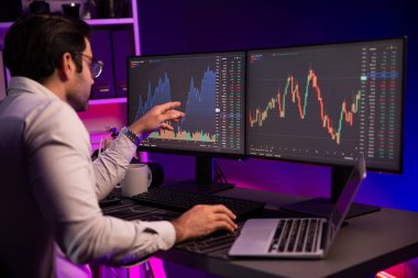 Akıllı tüccar işadamı, karanlık oda gecesinde neon ışıklı ofisteki arama pazarında yüksek kârla ekranda bilgisayar ve bilgisayar üzerinde dinamik borsa yatırımları üzerinde yoğunlaşıyor. Tahmin et..