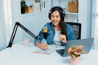 Sosyal medyada kulaklıkla canlı yayın yapan Asyalı sunucu modern stüdyoda yaşam koçluğu veya pazarlama dinleyicilerini selamlıyor. Taktik.