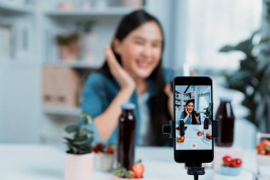 Seçici odaklı akıllı telefon ve gülümseyen genç, güzel Asyalı karışık çilek ve kiraz suyu detoksu değerlendirmesi sosyal medyada sağlıklı ürün tanıtımı sunuyor. Taktik.