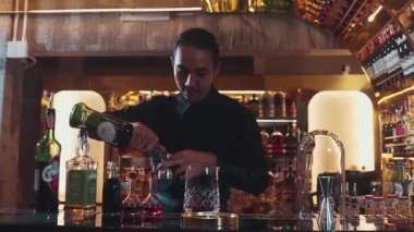 Güzel görünümlü Asyalı barmen içki şurubunu kullanarak lüks içki tezgahında cam hazırlama, gece kulübü lüksündeki düzgün profesyonel barmen kostümü yapıyor. Vinosity.