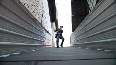 Genç gülümseyen iş adamının orta noktada dans edişinin düşük açılı görüntüsü. Takım elbise ve bavul giyip müziğe yönelen yetenekli bir yönetici. Müzikle ilgilenen mutlu yatırımcı. Sevinçli..