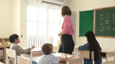 Çeşitli öğrenci ödevlerini kontrol ederken etrafta dolaşan ve etrafa bakan beyaz bir öğretmen. Çok kültürlü çocukların okuması ve dinlemesi ilkokuldaki sınıfta fikrini açıklıyor. Pedagoji.
