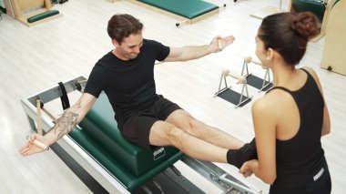 Beden eğitiminde birlikte pilates egzersizi yapan birkaç mutlu antrenör. Çekirdek gücü ve dengeyi arttırmak için reformcuda yüz poz veren İspanyol bir adam. Alışkanlık.