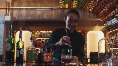 Zeki Asyalı barmen bardakta karıştırılmış alkol şurubunu buzla karıştırıyor. Çünkü kayanın üzerinde kamera var. Gece kulübünde taze kokteyl kokteylleri karıştırıyor. Vinosity.