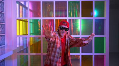 Komik break dansçı kameraya bakarken hiphop 'a doğru serbest adım atıyor. Çılgın mutlu hipster dans edip sokak dansı yaparken Led ışığında günlük kıyafet ve güneş gözlüğü takıyor. Mutluluk.