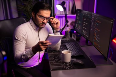 Akıllı bilişim geliştiricisi bilgisayar ekranında yazılım geliştirme kodlaması üzerinde çalışıyor ve en yeni uygulama projesinin notlarını okuyor, program güncellemesi düşünüyor neon ışıklı siber ofiste online web sitesi verileri. Tahmin et..