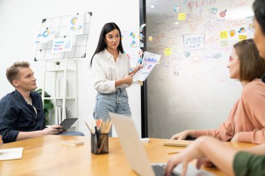 Güzel, genç, beyaz bir lider, modern iş toplantı odasındaki belgeye işaret ederken, profesyonel yatırımcılara grafik ve zihin haritası kullanarak yaratıcı pazarlama stratejisi sunuyor. Tertemiz..