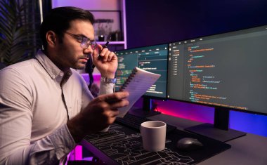 Akıllı bilişim geliştiricisi bilgisayar ekranında yazılım geliştirme kodlaması üzerinde çalışıyor ve en yeni uygulama projesinin notlarını okuyor, program güncellemesi düşünüyor neon ışıklı siber ofiste online web sitesi verileri. Tahmin et..