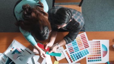 Akıllı tasarımcının renkli paletlerden renk seçmesine yardım ederken yukarıdan aşağı görünümü. Dizüstü bilgisayardan logoya bakarken birlikte çalışan ve planlayan iş adamlarının hava görüntüsü. Sempozyum.