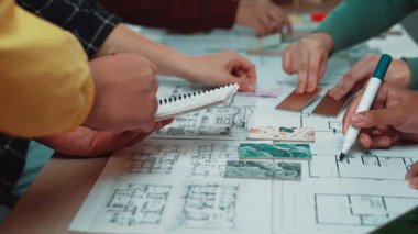 Tasarım modelleri, çizimler ve renkli malzemelerle kaplı bir masanın etrafında çeşitli ellerle yapılmış dinamik bir takım toplantısı, işbirlikçi bir çalışma ortamı sergiliyor. SACTR