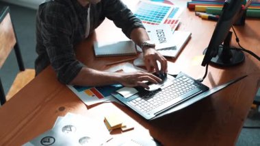 İç mimar dizüstü bilgisayarı, bilgisayarı ve kâğıdı olan toplantı masasında palete bakarken dizüstü bilgisayara bakıyor ve renk tasarlıyor. Renk tasarımı üzerinde çalışan iş adamına yakın çekim. Sempozyum.