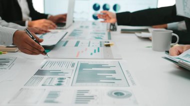 Çeşitli profesyonellerden oluşan bir grup, modern ofis ortamındaki dinamik bir toplantı sırasında çeşitli grafik ve grafikler kullanarak veri analizi üzerinde işbirliği yapmaktadır. SACTR