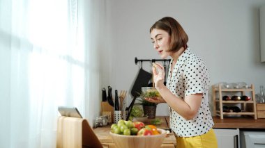 Kafkaseli anne kahvaltıda sebze pişirirken mutlu anne de modern mutfakta salata için taze malzemeler hazırlıyor. Hizmetçi sağlıklı yemek pişiriyor. Dikkat konsepti. Pedagoji.