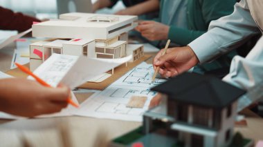 Dinamik bir mimari planlama oturumu, modeller ve çizimler üzerinde çalışan, canlı bir çalışma alanında yaratıcılık ve stratejik tasarım süreçleri sergileyen bir takım gösteriyor. SACTR