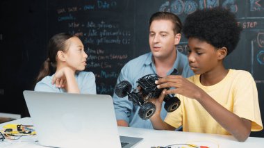 Akıllı öğretmen araba modelini farklı öğrencilere denetliyor. Karışık ırk dinleyicisi olan liseli çocuklar masadaki dizüstü bilgisayarlı ve kablolu robot model sistemini açıklıyor. Öğretim.