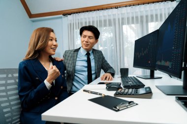 Başarılı gülümseyen Asyalı iş ortakları borsa veritabanında kârlı bir proje için el ele tutuşuyorlar. Yan görüntüdeki modern ev ofisinde resmi takım elbise giyiyorlar. İnfobahn.